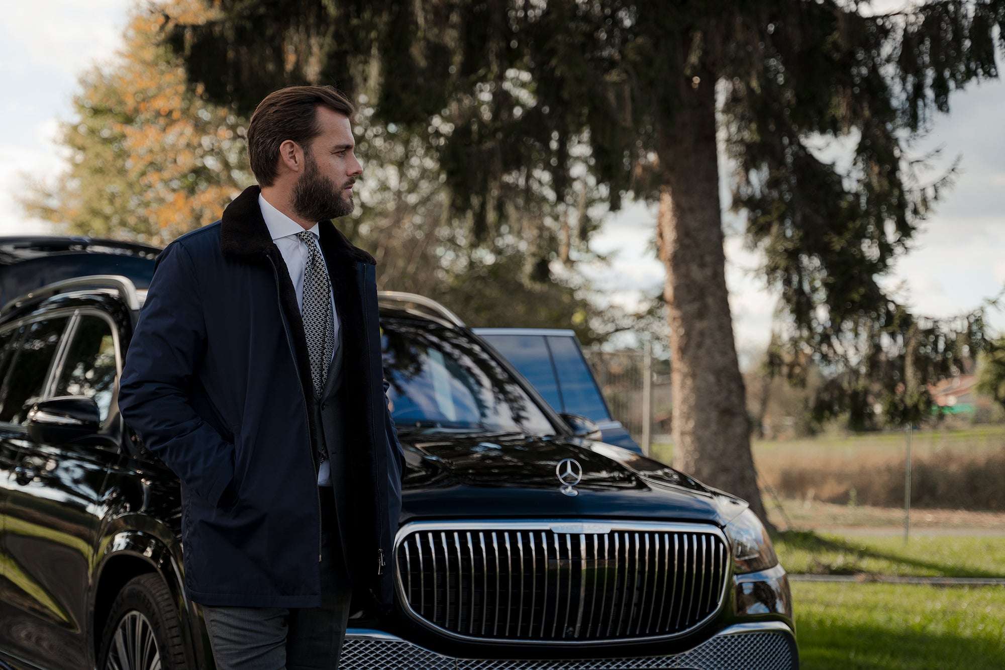 Man standing next to a black Maybach in a park-like setting